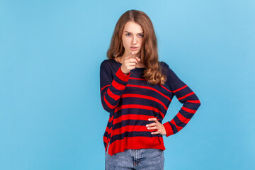 Hey you, be careful! Portrait of young woman wearing striped casual style sweater seriously pointing finger and looking at camera, warning. Indoor studio shot isolated on blue background.