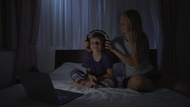 A woman at night turns on a meditation, relaxation application on her computer for her son to relax before going to bed. Antistress apps. Healthy lifestyle. New normal