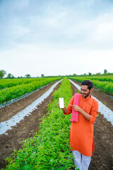 Young indian farmer showing smartphone screen at agriculture field.