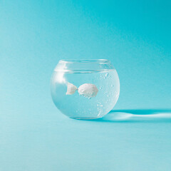 Creative composition with fish bowl and candy wraped in white plastic against blue background....