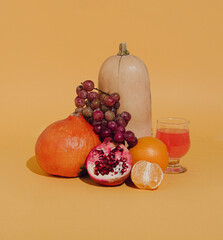 Minimal retro arrangement with pumpkin, grapes, and glass of drink. Creative autumn background idea.