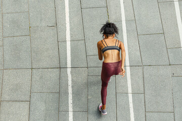 Young biracial woman in stylish sportswear runs along empty stadium track upper view. Development and achievement concept