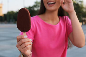 Young woman holding ice cream glazed in chocolate on city street, closeup