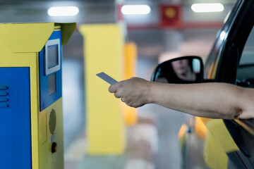 Woman driving her car brings the card to enter the parking lot to the control machine and open the barriers. View from behind.