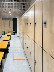 Beige lockers with an orange bench in a locker room of a sports club.