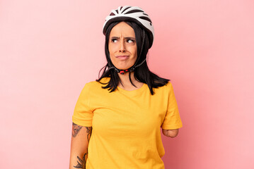 Young caucasian woman with one arm wearing a bike helmet isolated on pink background confused, feels doubtful and unsure.