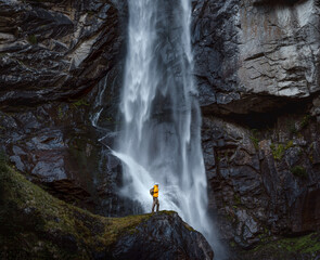 Backpacker man in yellow jacket explores waterfall in Switzerland