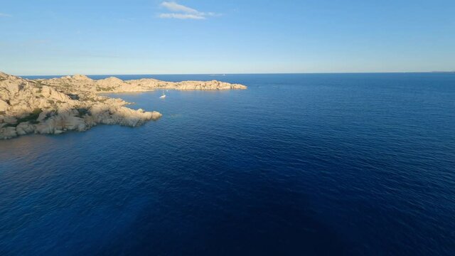 FPV video, flying at high speed over a granite coast with a turquoise bay of water. Cala Coticcio (Tahiti) La Maddalena archipelago, Sardinia, Italy.