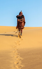 Himba woman in traditional dress is walks through the desert.