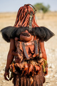 Himba tribe woman with a child behind her back in traditional dress.