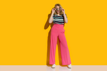 Stylish young woman in pink baggy pants is posing and looking over sunglasses. - 465013011