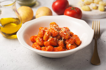 Traditional gnocchi with tomato sauce and cheese in a white plate with ingredients on a table