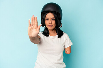 Young caucasian woman with one arm wearing a motorcycle helmet isolated o blue background standing with outstretched hand showing stop sign, preventing you.