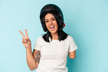 Young caucasian woman with one arm wearing a motorcycle helmet isolated o blue background joyful and carefree showing a peace symbol with fingers.