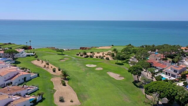 Aerial overview of Quinta do Lago resort buildings in Vale de Lobo, Algarve, Portugal, Europe. Shot of rooftops of luxury cottages in green landscape with mountains on background. Golf fields.