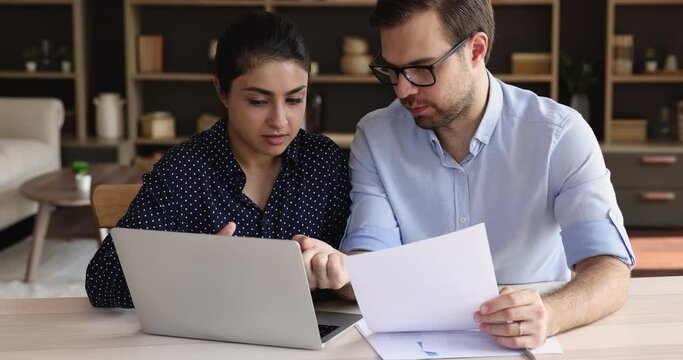 Coaching on workplace. Focused young man project coordinator engaged in paperwork with indian woman staff member by laptop screen. Skilled male mentor share experience give advice to female apprentice