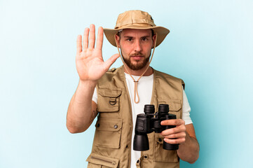 Young caucasian man looking at animals through binoculars isolated on blue background smiling cheerful showing number five with fingers.