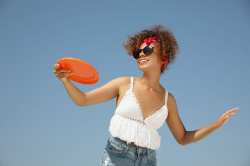Happy African American woman throwing flying disk against blue sky on sunny day