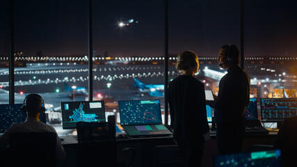 Female and Male Air Traffic Controllers with Headsets Talk in Airport Tower at Night. Office Room...