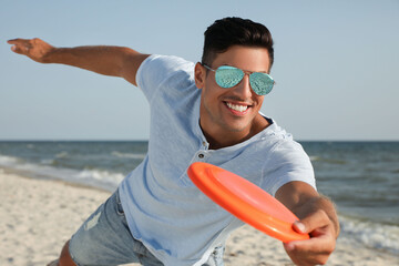 Happy man throwing flying disk at beach on sunny day