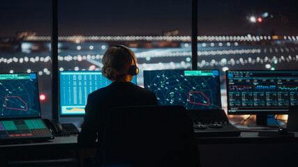 Female Air Traffic Controller with Headset Talk on a Call in Airport Tower at Night. Office Room is Full of Desktop Computer Displays with Navigation Screens, Airplane Flight Radar Data for the Team. © Gorodenkoff
