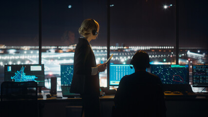 Female and Male Air Traffic Controllers with Headsets Talk in Airport Tower at Night. Office Room Full of Desktop Computer Displays with Navigation Screens, Airplane Flight Radar Data for Controllers.