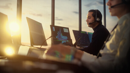 Male Air Traffic Controller with Headset Talk on a Call in Airport Tower. Office Room is Full of Desktop Computer Displays with Navigation Screens, Airplane Departure and Arrival Data for the Team. © Gorodenkoff