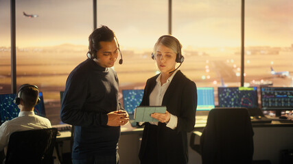 Female and Male Air Traffic Controllers with Headsets Talk in Airport Tower. Office Room Full of...