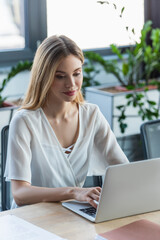 Fototapeta premium Pretty businesswoman using laptop near paper folder in office