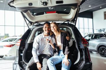 Couple sitting in open trunk of new auto and holding keys