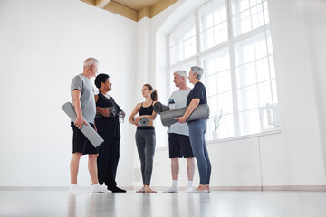 Seniors people discussing sports training together with their coach while they standing in big light studio