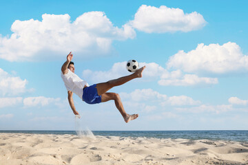 Man kicking football ball on beach near sea