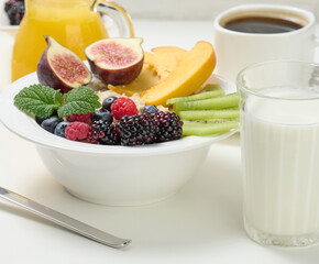 full plate with oatmeal and fruit, freshly squeezed juice in a transparent glass decanter, cup of coffee on a white table. Healthy breakfast