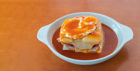 Hot Francesinha sandwich with sausages and meat, melted cheese, poured with beer sauce and topped with a fried egg. Close up in a plate on the table.