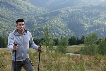 Tourist with trekking poles hiking through mountains, space for text