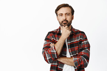 Image of thoughtful caucasian man looking serious at camera, thinking, making his decision at shop, standing over white background