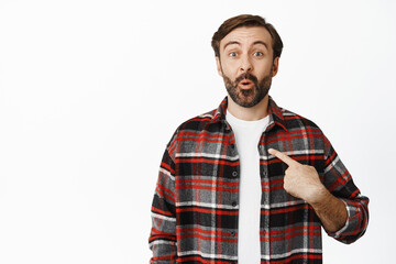 Surprised bearded man pointing at himself and rejoicing, being chosen, winning something, standing over white background