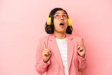 Young latin woman listening to music isolated on pink background pointing upside with opened mouth.