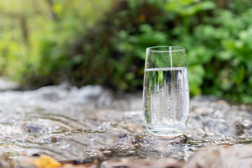 a glass of clean transparent drinking water in a transparent glass on a stone in a green forest near a stream or mountain spring. healthy food and diet, beautiful background copy space