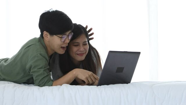 Happy Asian lesbian couple leisure activity concept, elder glasses female touch younger woman using laptop on bed