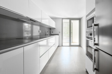 View of a kitchen with white cabinets, gray synthetic stone countertop and stainless steel appliances with black hob and exit to a terrace to dry clothes