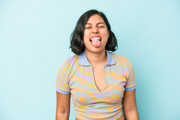 Young latin woman isolated on blue background funny and friendly sticking out tongue.