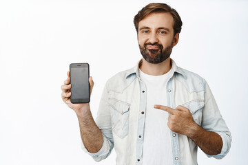 Disappointed guy pointing at mobile phone screen and grimacing, express dislike and bad opinion,...