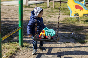 happy joyful kid is playing at playground area with toy plastic truck and swings.swing with massive...