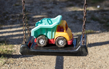 plastic toy truck on bench,wooden fence,swing for kids or blue old slide,peeled paint.one left toy for kid,little boy,abandoned.forgotten toy awaiting the child owner.orange,red,blue.autumn sunny day,