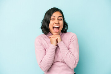 Young latin woman isolated on blue background praying for luck, amazed and opening mouth looking to front.