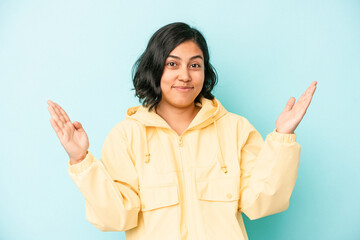 Young latin woman isolated on blue background holding something little with forefingers, smiling and confident.