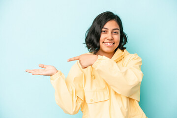 Young latin woman isolated on blue background excited holding a copy space on palm.