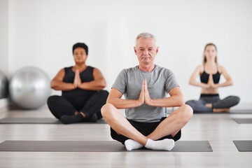 Obraz premium Portrait of senior man sitting in lotus position and meditating during yoga class in studio