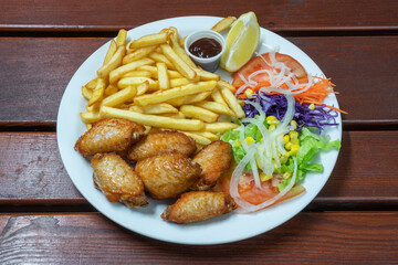 Grilled chicken legs in sauce and garnished with fried potatoes and vegan salad. On a wooden background, close-up.